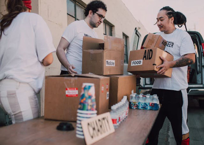 Volunteers in white shirts packing and organizing boxes of food and medicine labeled for aid at a charity distribution site to encourage people to donate.